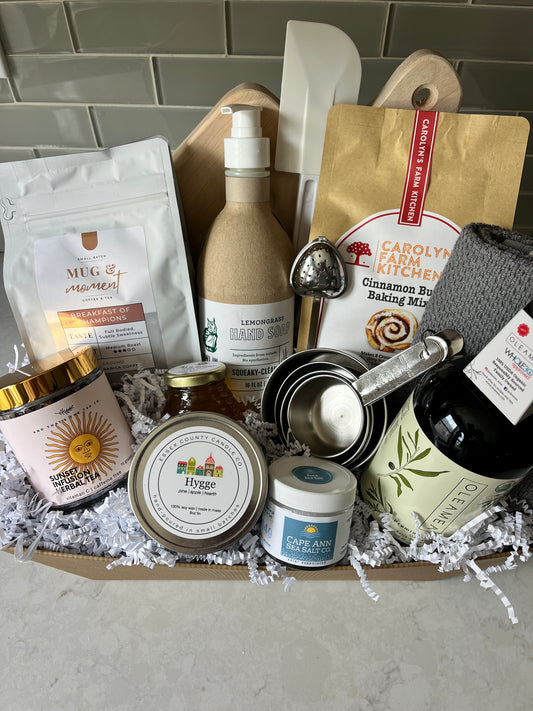 "Everything But The Kitchen Sink Gourmet Gift Basket with cutting board, olive oil, sea salt, hand soap, cookie, towel, spatula, measuring cups, tea, honey, coffee, baking kit, and candle"